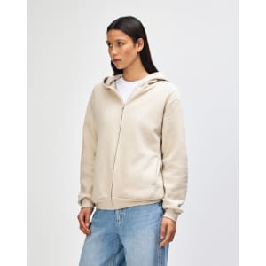 A unisex full zip hooded sweatshirt in a light beige colour, featuring a hood and a zip closure, shown on a model.