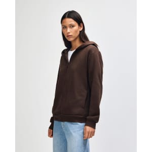 A unisex full zip hooded sweatshirt in brown, featuring a front zipper and a hood. The model stands with hands in pockets.