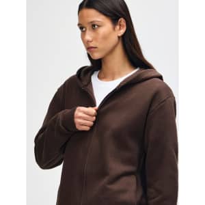 A brown unisex full zip hooded sweatshirt displayed on a model with curly hair. The sweatshirt has a logo.