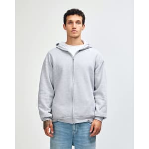 A unisex full zip hooded sweatshirt in heather grey with a hood and pockets. The model stands with hands in pockets.