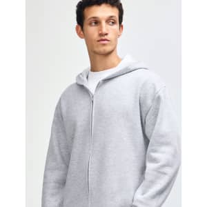 A unisex full zip hooded sweatshirt in grey, featuring a logo and paired with light blue jeans.