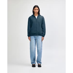 A unisex full zip hooded sweatshirt in navy, worn with baggy light blue jeans. Features a logo on the front.