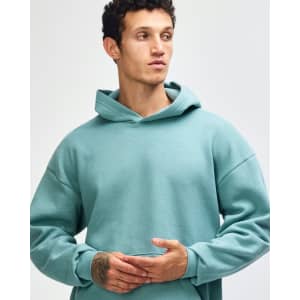 A unisex hooded sweatshirt in a soft green shade, featuring a relaxed fit and a front pocket. It has a logo.