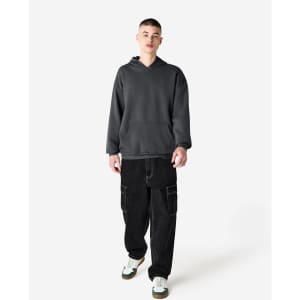 A unisex hooded sweatshirt in dark grey, worn by a model with baggy black trousers and white sneaker accents.