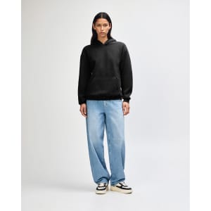 A unisex black hooded sweatshirt is worn with light blue baggy jeans and black sneakers, featuring a logo.