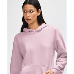 A unisex hooded sweatshirt in soft pink, featuring a front pocket and a branding logo.