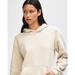 A unisex hooded sweatshirt in a light cream colour, featuring a front pocket and a logo.