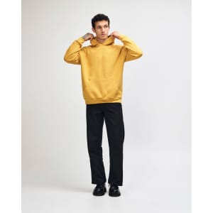 A unisex hooded sweatshirt in mustard yellow with a front pocket and a relaxed fit, featuring a logo.