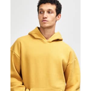 A unisex hooded sweatshirt in a warm gold colour, featuring a front pocket and a relaxed fit. It has a logo.