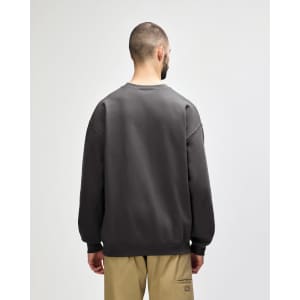 A back view of a woman wearing an olive green Gildan Softstyle adult sweatshirt with a logo.