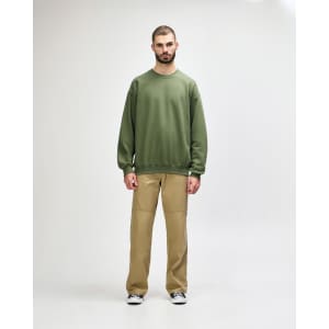 A green Gildan Softstyle adult sweatshirt worn by a model, paired with dark pants and black sneakers.