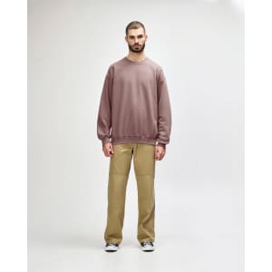 A male model wears a dusty pink Gildan Softstyle Adult Sweatshirt with black pants and black sneakers. The sweatshirt has a simple design.