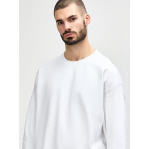 A white Gildan Softstyle adult sweatshirt is worn by a model with dark hair, featuring a relaxed fit and long sleeves.