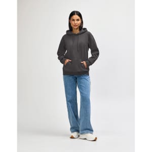 A woman wears a grey hooded sweatshirt with a logo, paired with denim jeans and white sneakers.