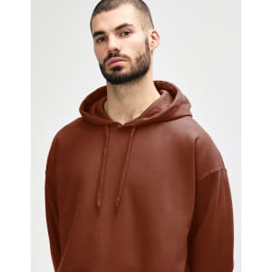 A woman wearing a brown Gildan Softstyle adult hooded sweatshirt, holding the hood with both hands.