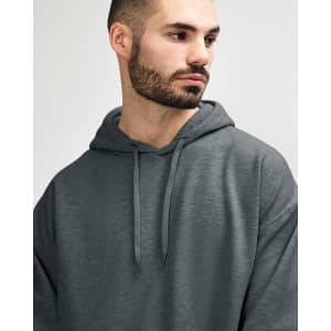 A soft grey hooded sweatshirt, featuring a front pocket and a hood, worn by a model. It has a small logo.