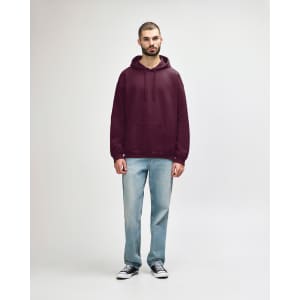 A woman is wearing a burgundy hooded sweatshirt paired with blue jeans and white sneakers. The sweatshirt has a logo.