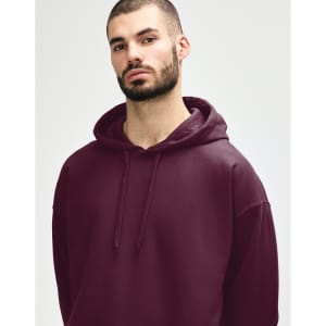 A woman models a burgundy Gildan Softstyle adult hooded sweatshirt with a drawstring hood and a subtle logo.