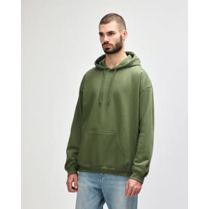 A green Gildan Softstyle adult hooded sweatshirt worn by a model, featuring a front pocket and a drawstring hood.