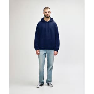 A model wearing a navy hooded sweatshirt and blue jeans, featuring a front pocket and a logo.