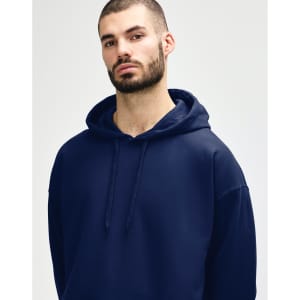 A woman wearing a navy blue hooded sweatshirt, with a relaxed expression, holding the hood. The sweatshirt has a logo.