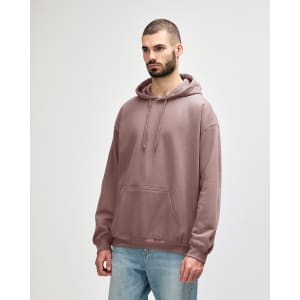 A person stands wearing a pink hooded sweatshirt with a front pocket and a drawstring hood.