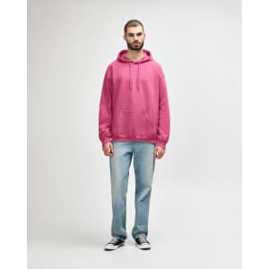A pink hooded sweatshirt featuring a front pocket, paired with blue jeans and white sneakers.