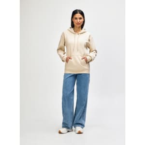 A hooded sweatshirt in cream worn by a person, paired with blue jeans and white shoes. The sweatshirt has a logo.