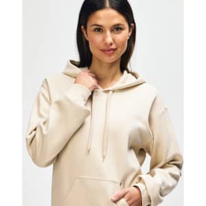 A model wearing a beige Gildan Softstyle adult hooded sweatshirt with the hoodie drawn over her head.