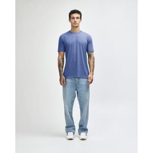 A man wearing a blue American Apparel tri-blend T-shirt and light blue jeans, standing against a plain background.