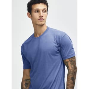 A blue tri-blend t-shirt on a model with tattoos, featuring a simple design and a logo.