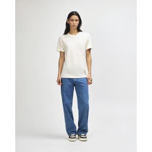 A plain cream tri-blend t-shirt is worn with blue denim pants, featuring a simple design and a logo.