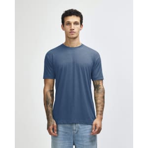 A blue American Apparel tri-blend T-shirt displayed on a model with tattoos, paired with denim jeans.