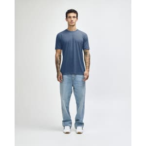 A man wearing a blue American Apparel Tri-Blend T-Shirt paired with light blue jeans and white sneakers.