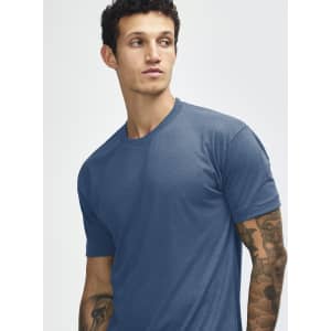 A blue American Apparel tri-blend t-shirt worn by a person with tattoos. The shirt has a round neck and short sleeves.
