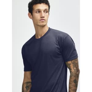 A navy blue tri-blend T-shirt displayed on a model with tattoos, featuring a simple design and a logo.