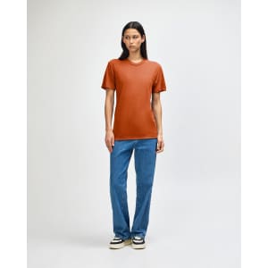 A model wearing an orange American Apparel Tri-Blend T-Shirt paired with blue jeans. The shirt has a logo.