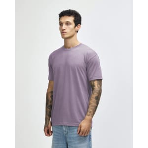 A man wears a purple American Apparel tri-blend t-shirt paired with light denim jeans. The shirt has a casual fit.