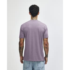 A tri-blend t-shirt in a muted purple colour, viewed from the back, worn by a person with tattoos.