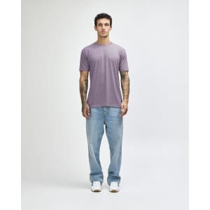 A model wearing a lavender American Apparel Tri-Blend T-Shirt paired with light blue jeans and white sneakers.