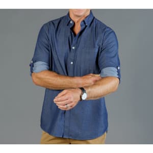 A button-up shirt in navy chambray with rolled sleeves and a subtle pattern. It features a logo on the chest.