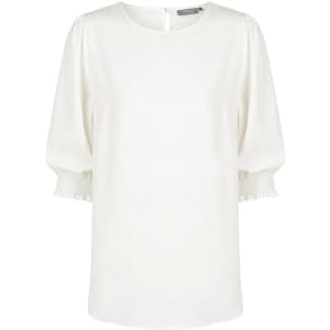 A white blouse with shirred cuffs and a round neckline, featuring a button closure at the back and a brand logo.