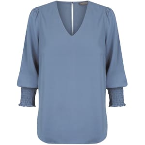 A blue Cleo V Neck shirt with long, puffed sleeves and smocked cuffs. It features a deep V-neckline and branding.