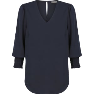 A navy V-neck shirt with puff sleeves and smocked cuffs, featuring a logo at the neckline.