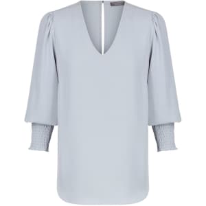 A light blue V-neck shirt with puffed sleeves and smocked cuffs, featuring a back slit detail. It has a logo.