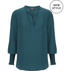 A teal long sleeve top features a mandarin collar and smocked sleeves, complemented by a logo.
