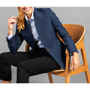 A blue jacket displayed on a seated model, paired with a light-coloured shirt and black pants, featuring a logo.