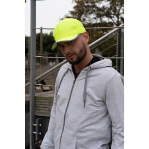 A man wearing a bright yellow cap stands outdoors, paired with a grey hoodie. The cap features reflective trim and a logo.