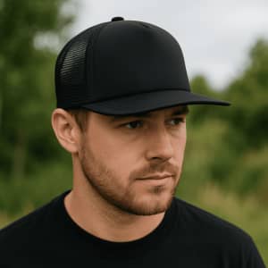 A black flat peak trucker mesh cap with a solid front and mesh back, worn by a man in a natural setting.