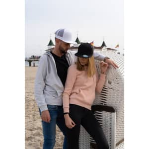 A grey hoodie and a black snapback cap on a male model, alongside a female model in a pink hoodie and black cap, both at the beach.